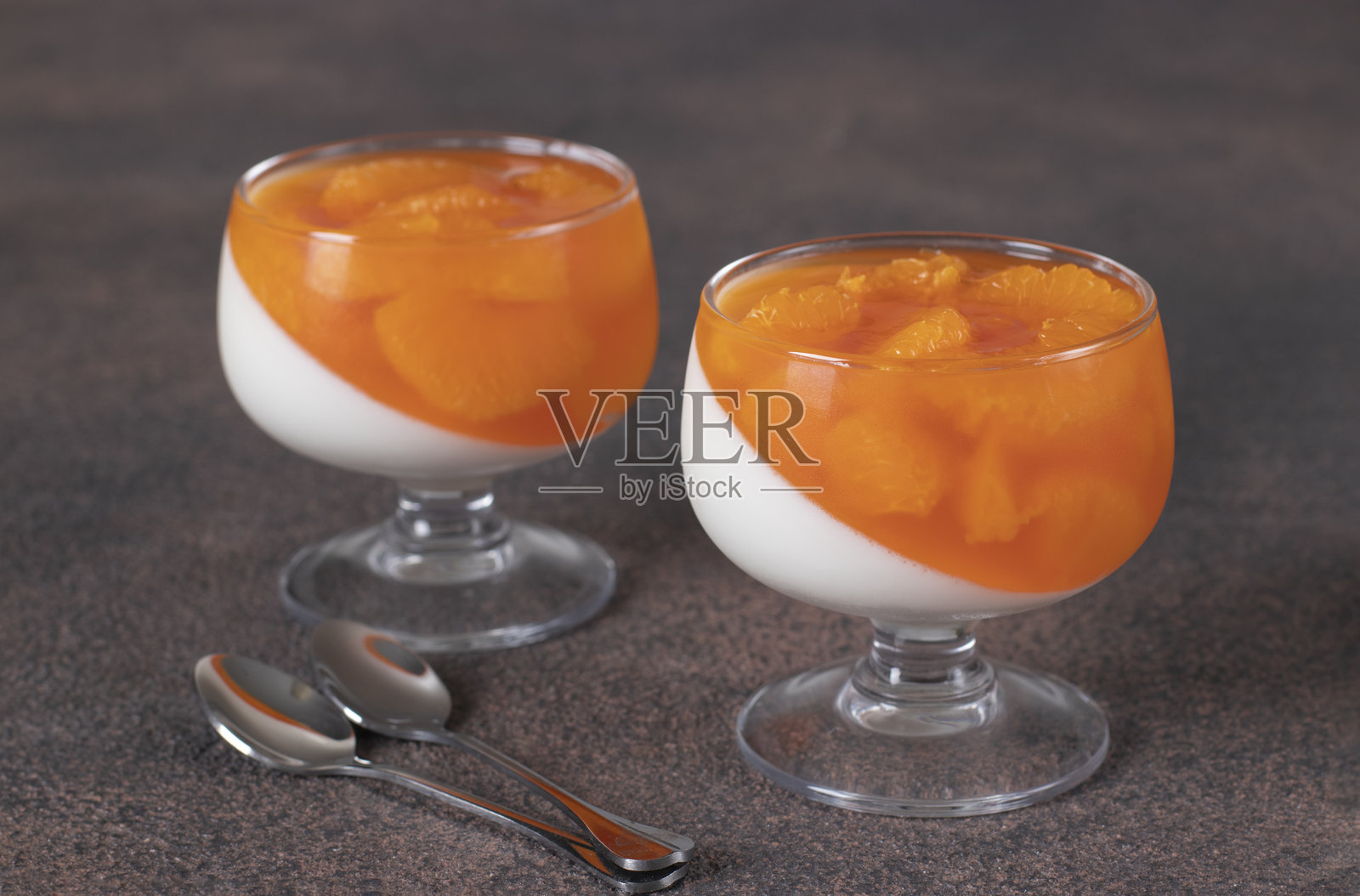 两杯橘子奶冻甜点置于棕色背景上照片摄影图片