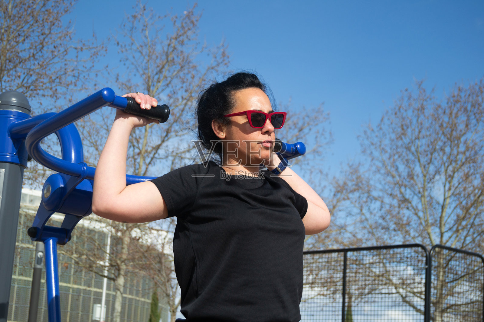 阳光明媚的日子里，女性在户外健身器材上锻炼照片摄影图片