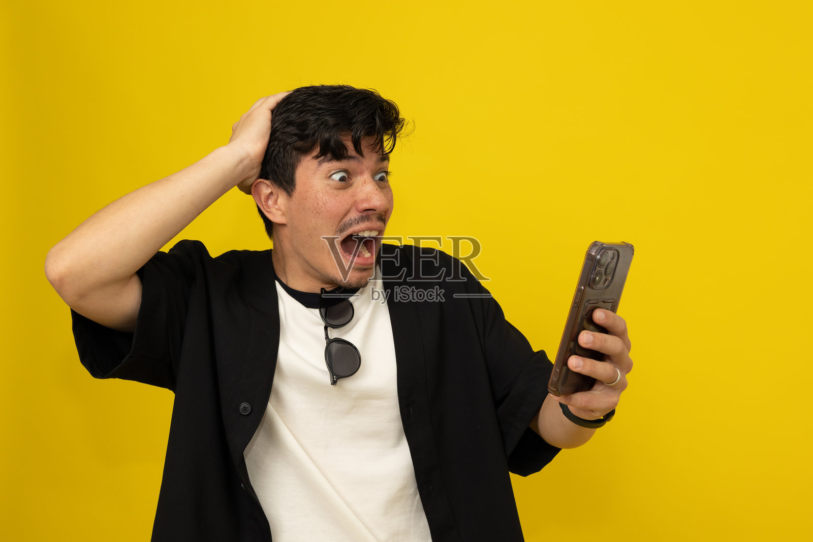 年轻男子在黄色背景下看着手机，面露惊恐表情，旁边留有空白空间。照片摄影图片