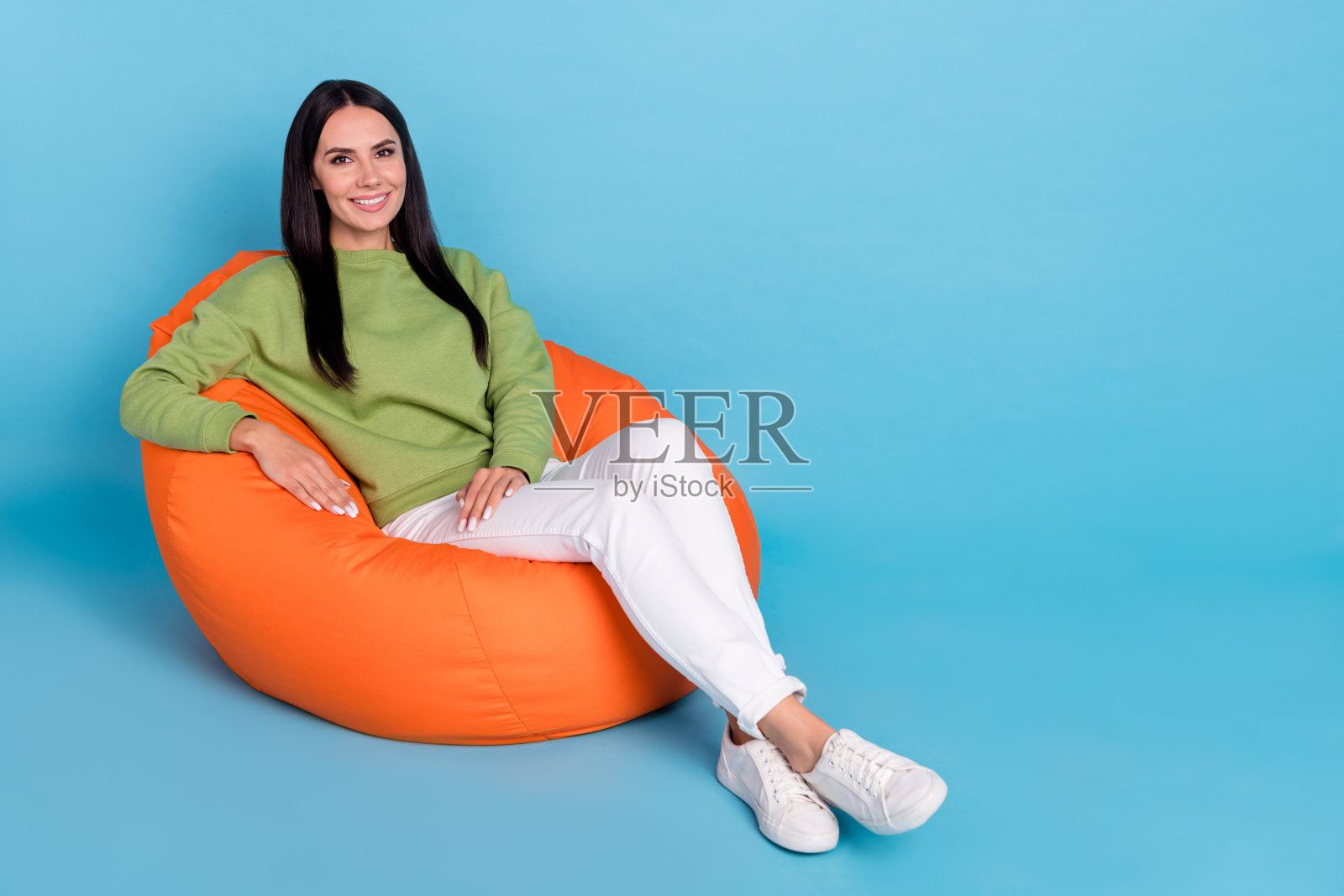 坐在大软椅上的迷人友好人士，露出灿烂的微笑，背景为蓝色。照片摄影图片