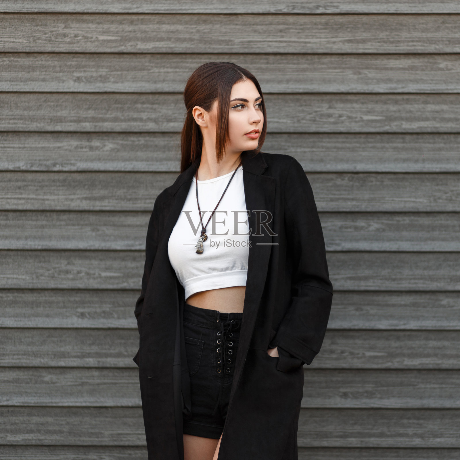 身穿黑色外套的美丽年轻女性模特站在一座木屋旁。照片摄影图片