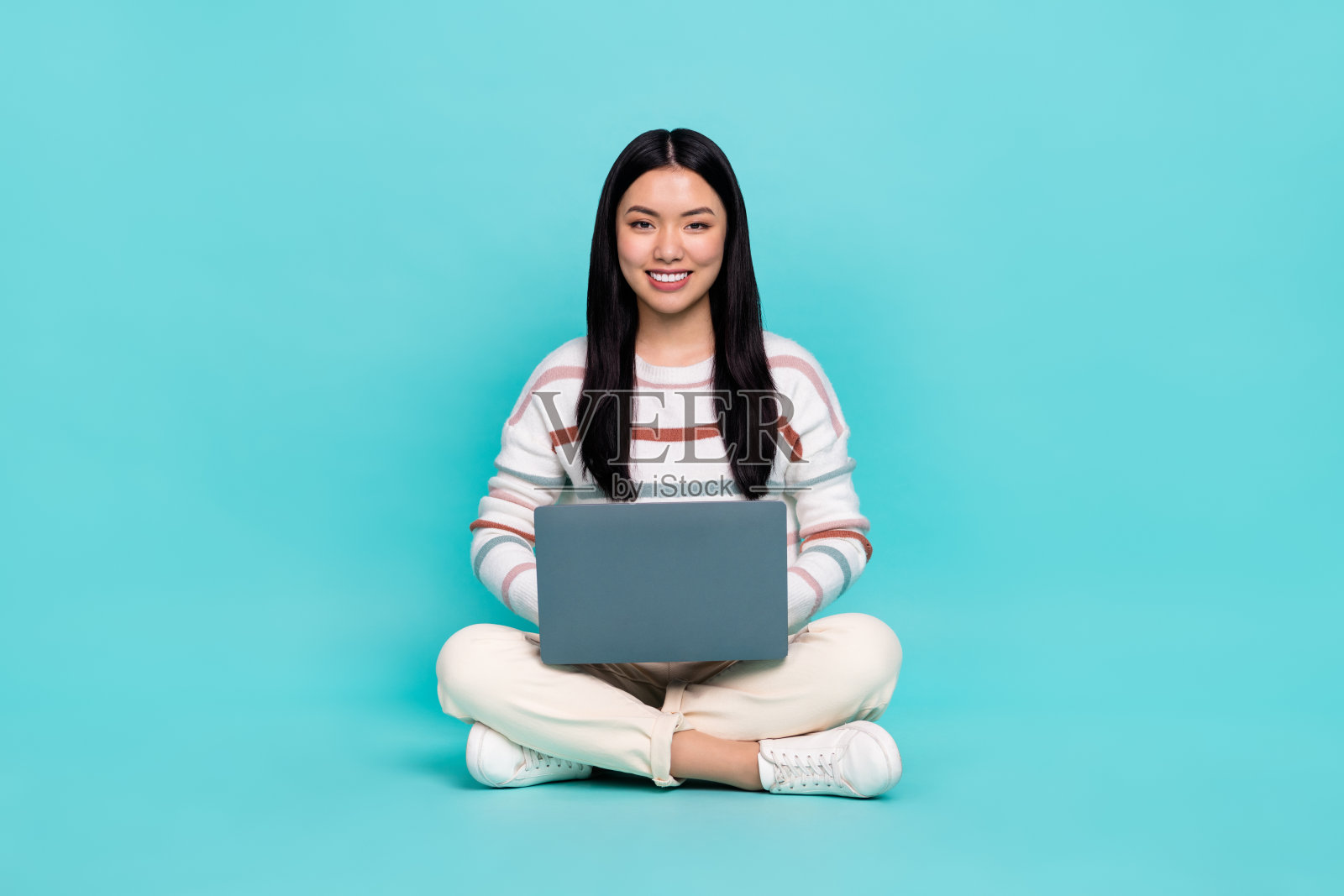 迷人的自由职业女性在青色背景下使用笔记本电脑写电子邮件和制作演示文稿。照片摄影图片