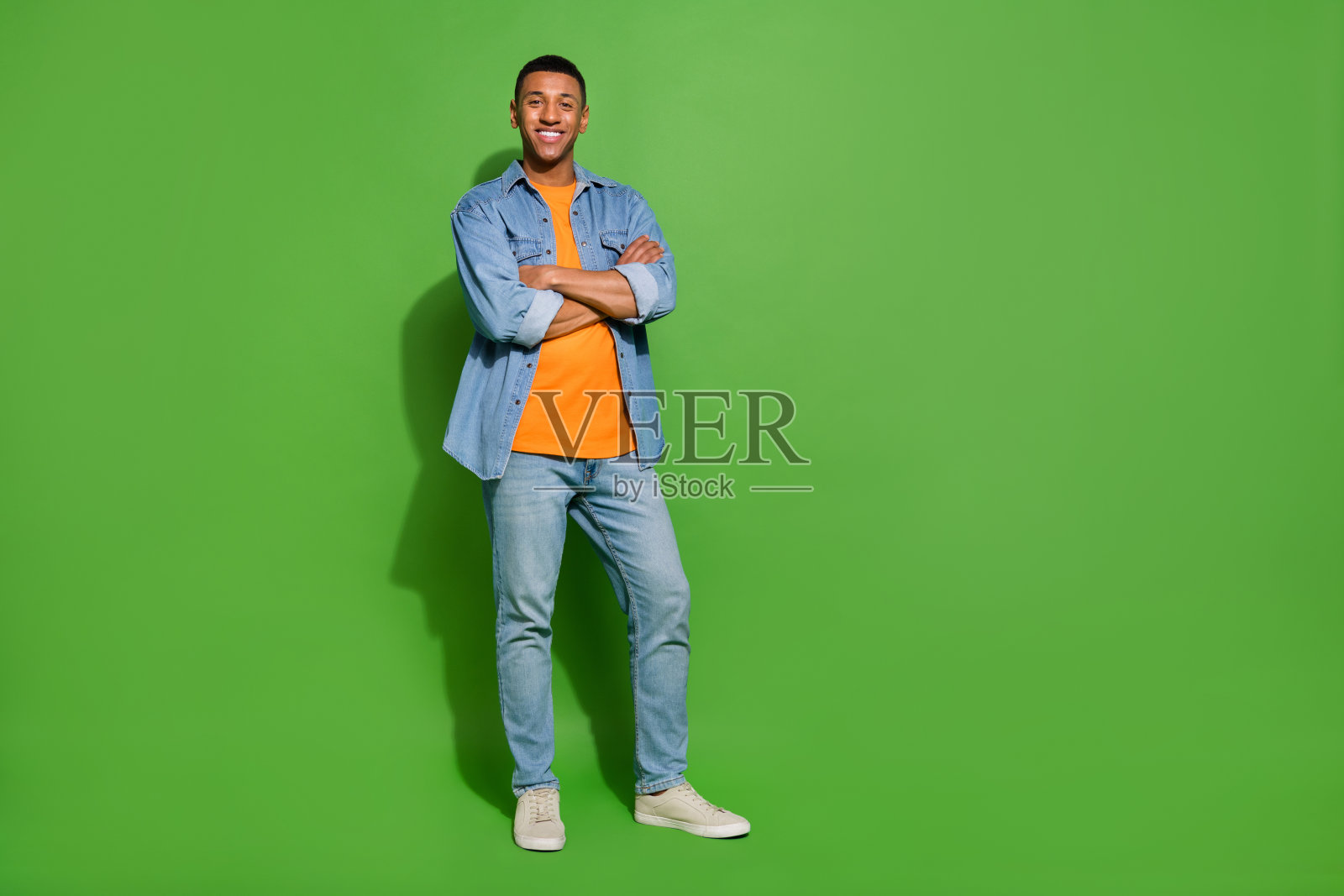 年轻聪明的企业家全身照，双手交叉，背景为绿色。照片摄影图片