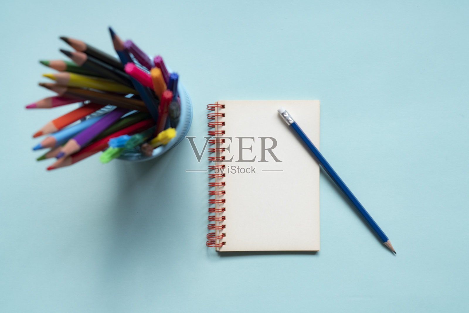 蓝色背景上有铅笔盒里的彩色铅笔和一个记事本照片摄影图片