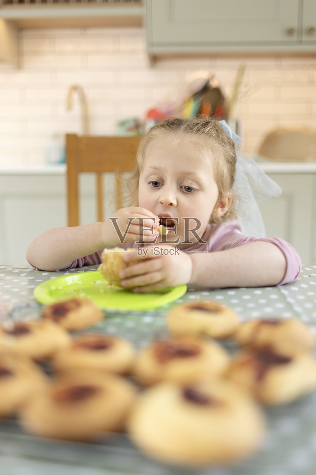 可爱的4岁女孩正在吃一块新鲜自制的果酱饼干，其余的饼干正在铁架上冷却。照片摄影图片