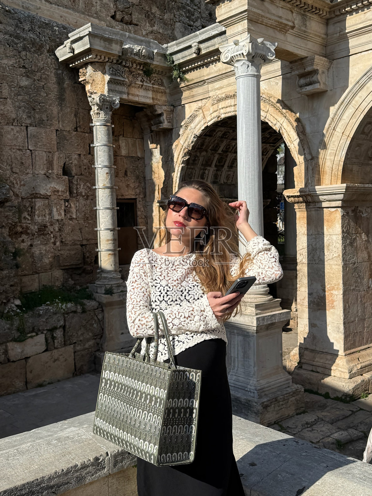 年轻女性在历史遗址享受阳光明媚的下午，同时使用她的智能手机。照片摄影图片