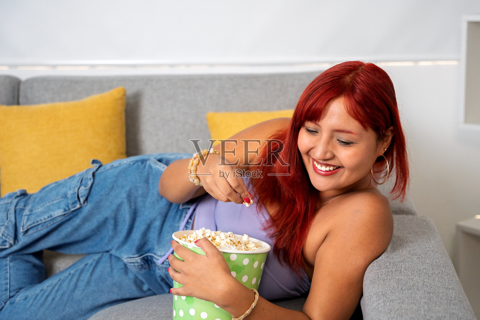 年轻女性在沙发上放松，享受电影和爆米花，同时使用移动科技照片摄影图片