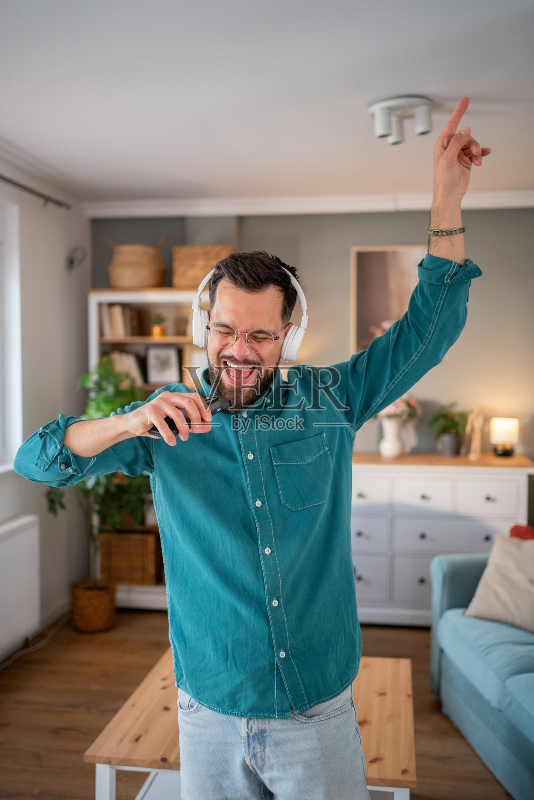 热情的男子在家中戴着耳机和智能手机唱歌照片摄影图片