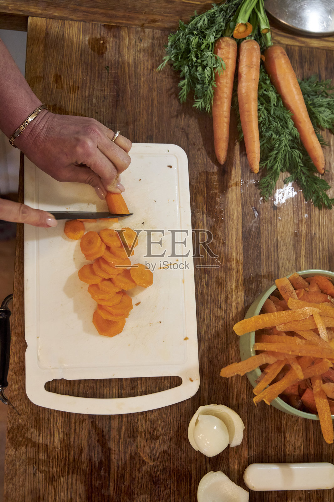 从上方俯视一位女性的手，正在乡村风格的木质厨房台面上小心地切割新鲜胡萝卜。照片摄影图片