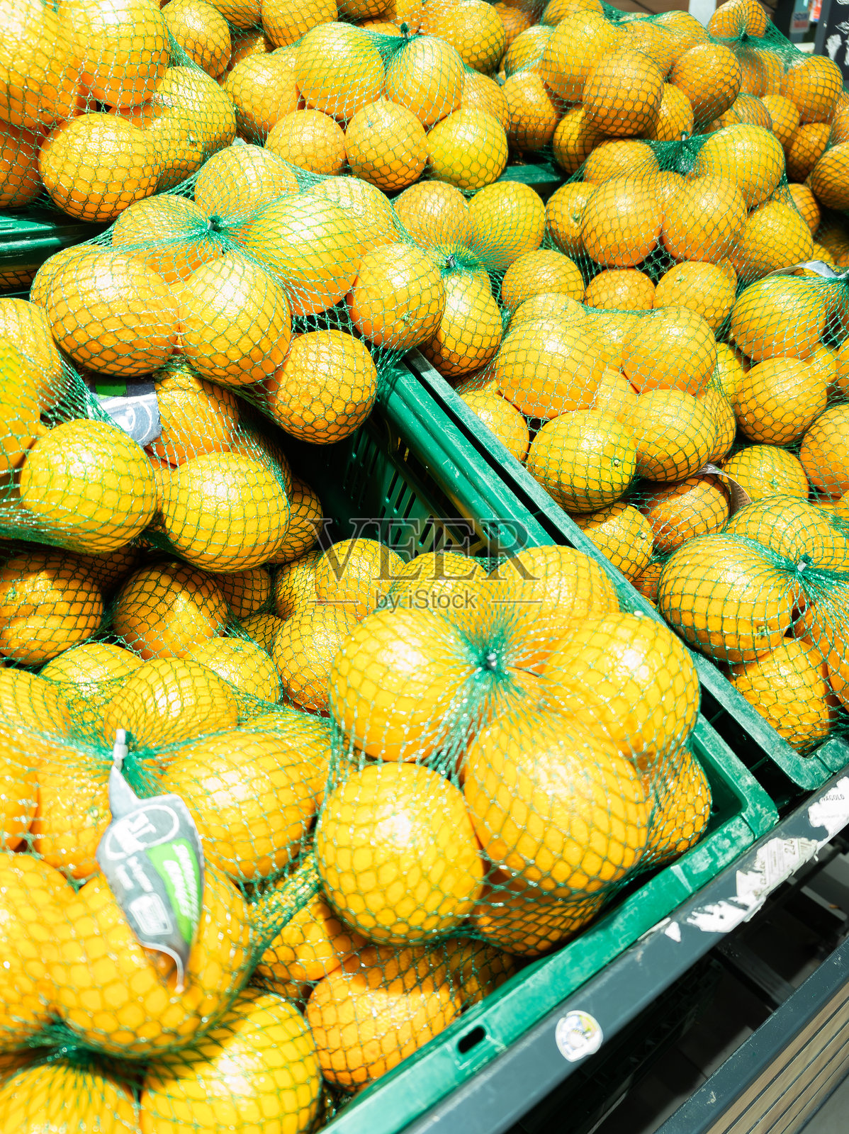商店水果和蔬菜部门出售的橙子。橙子装在绿色网袋中，放在绿色塑料箱里。照片摄影图片