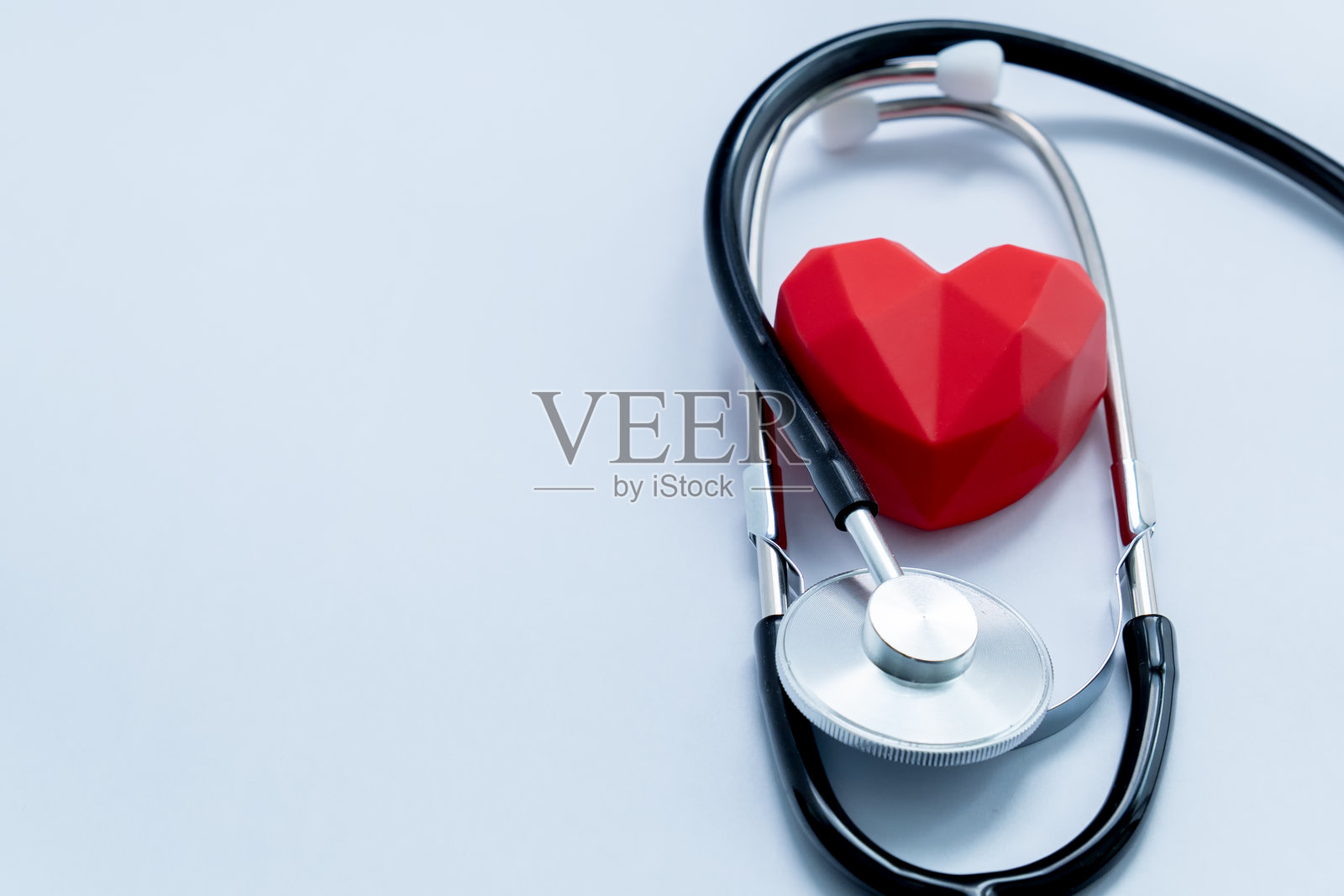 听诊器环绕着一个红色多边形心脏，象征着医疗和心脏病学，留有文本空间照片摄影图片
