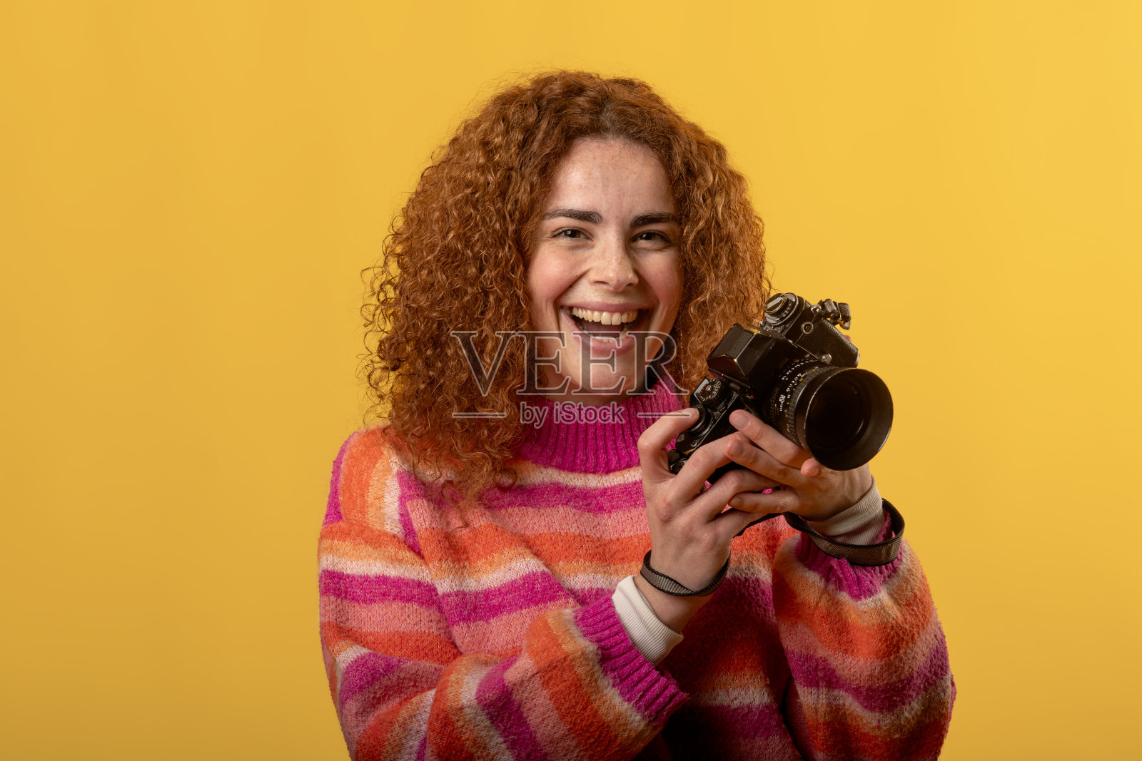 年轻摄影师在摄影棚中笑着，手里拿着一台复古相机照片摄影图片