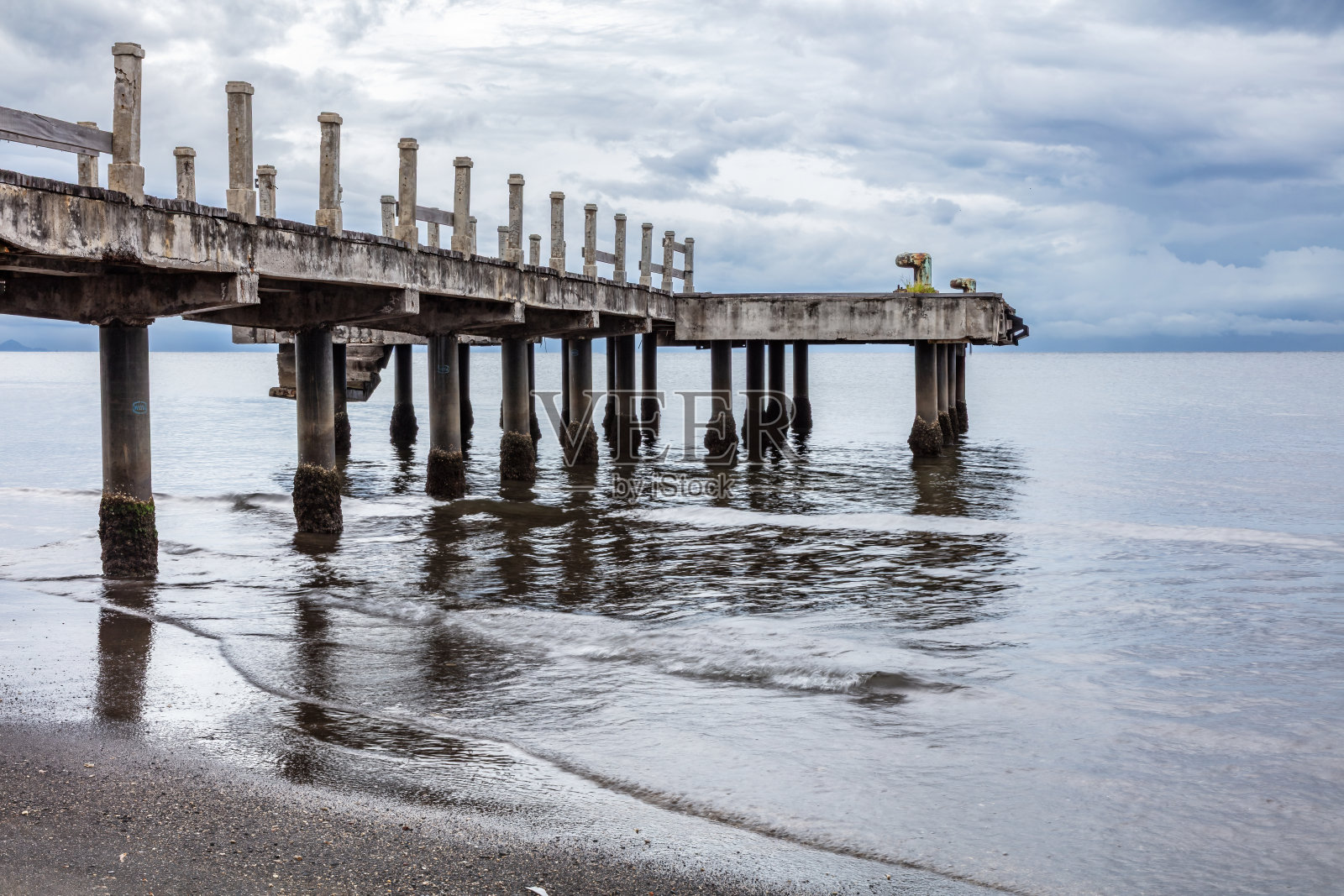 木栈道；平静的水面，前景是沙滩，头顶是多云的天空。照片摄影图片
