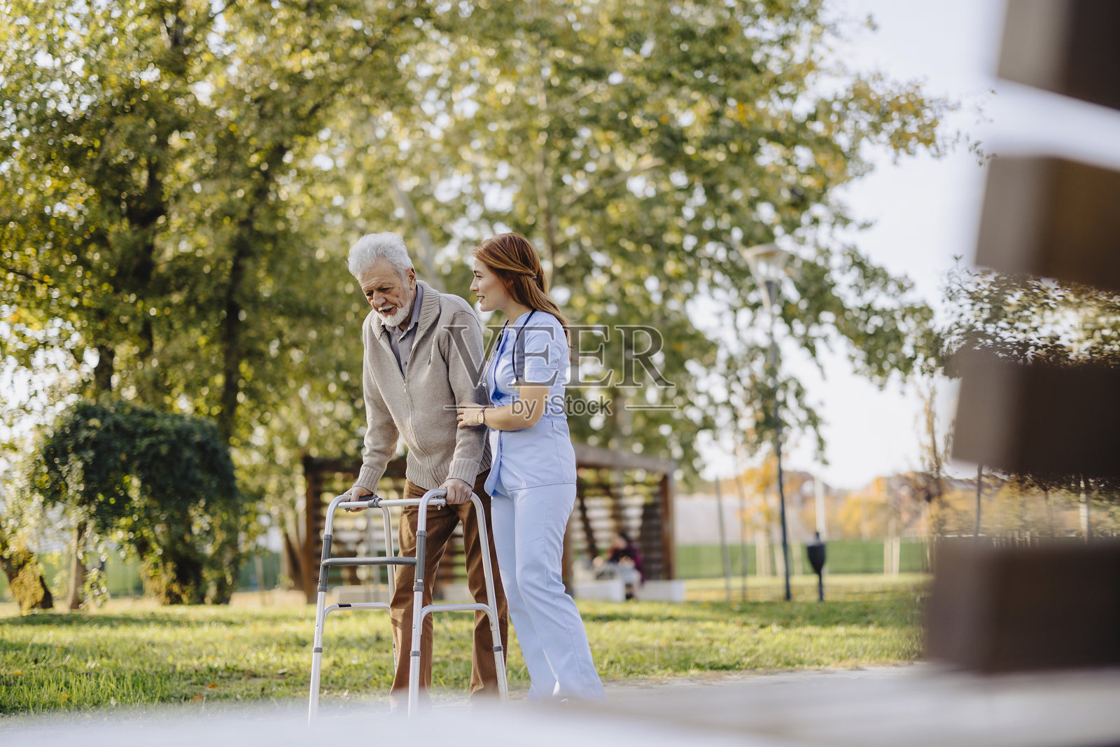 女性护士或医生在户外帮助老年患者使用矫形助行器练习走路，患者在花园中与物理治疗师一起练习行走，照顾居家老年人，医疗健康。照片摄影图片
