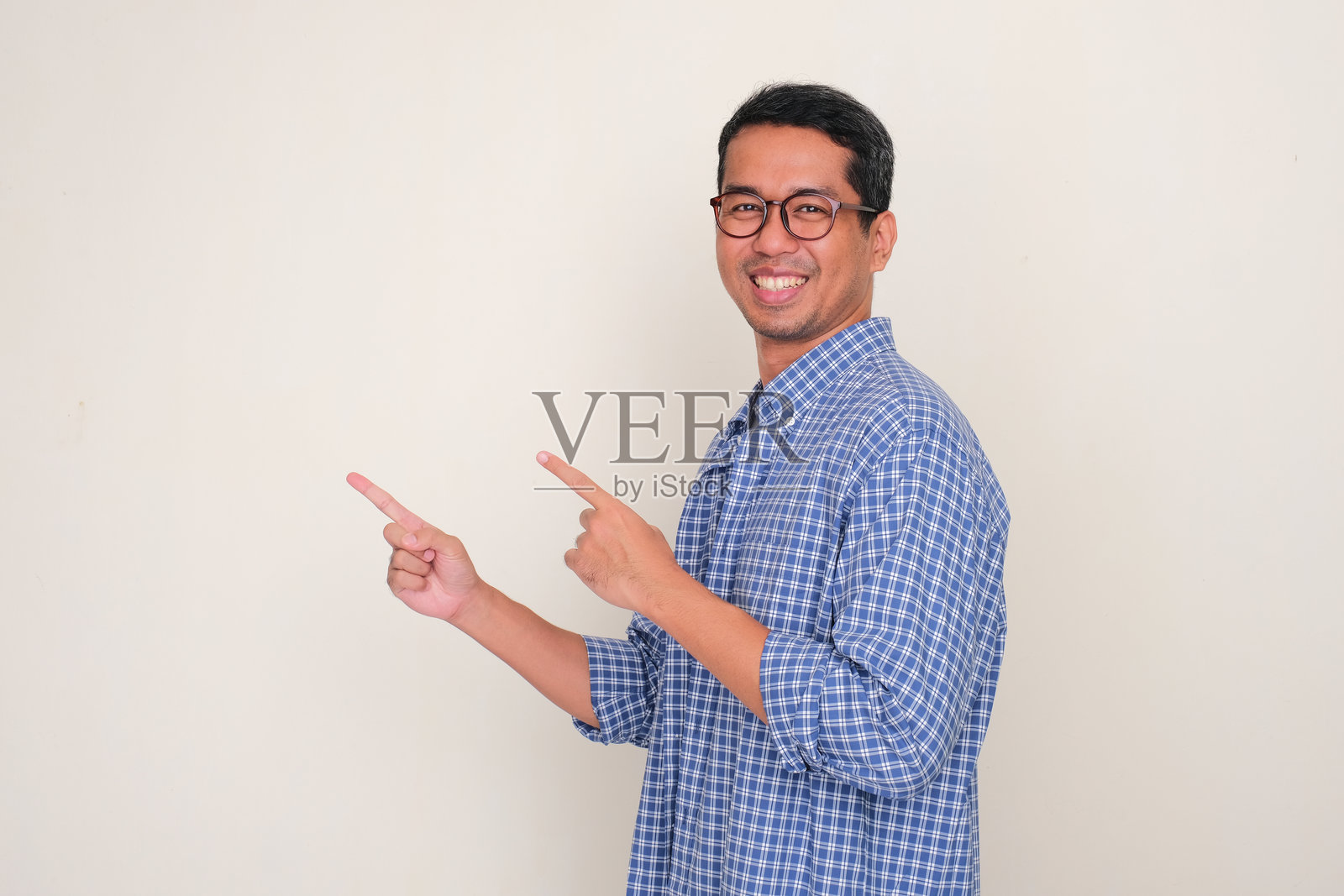 侧面视角的成年亚洲男子微笑，双手指向旁边。照片摄影图片