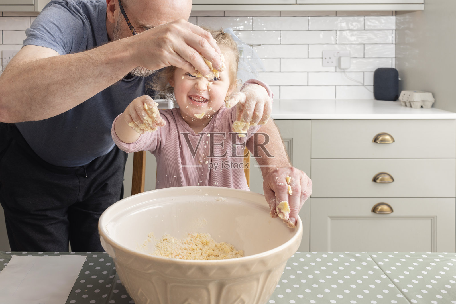 祖父在厨房桌子上监督孙女一起搅拌大碗里的饼干面团，准备烤自制果酱饼干。照片摄影图片