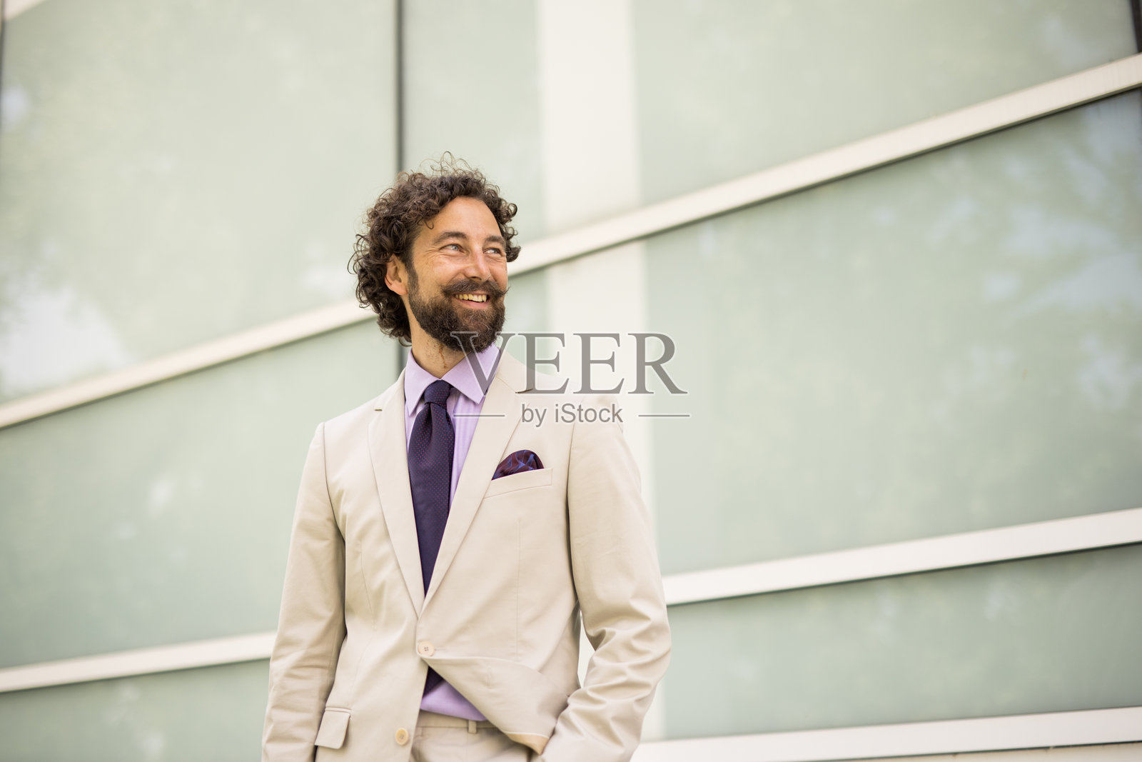 微笑的商人站在办公楼旁，目光投向远方。照片摄影图片