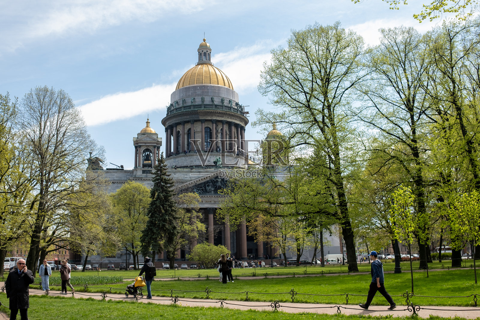 游客在圣彼得堡的圣以撒大教堂附近享受阳光明媚的一天，周围是郁郁葱葱的绿树和盛开的花园。照片摄影图片