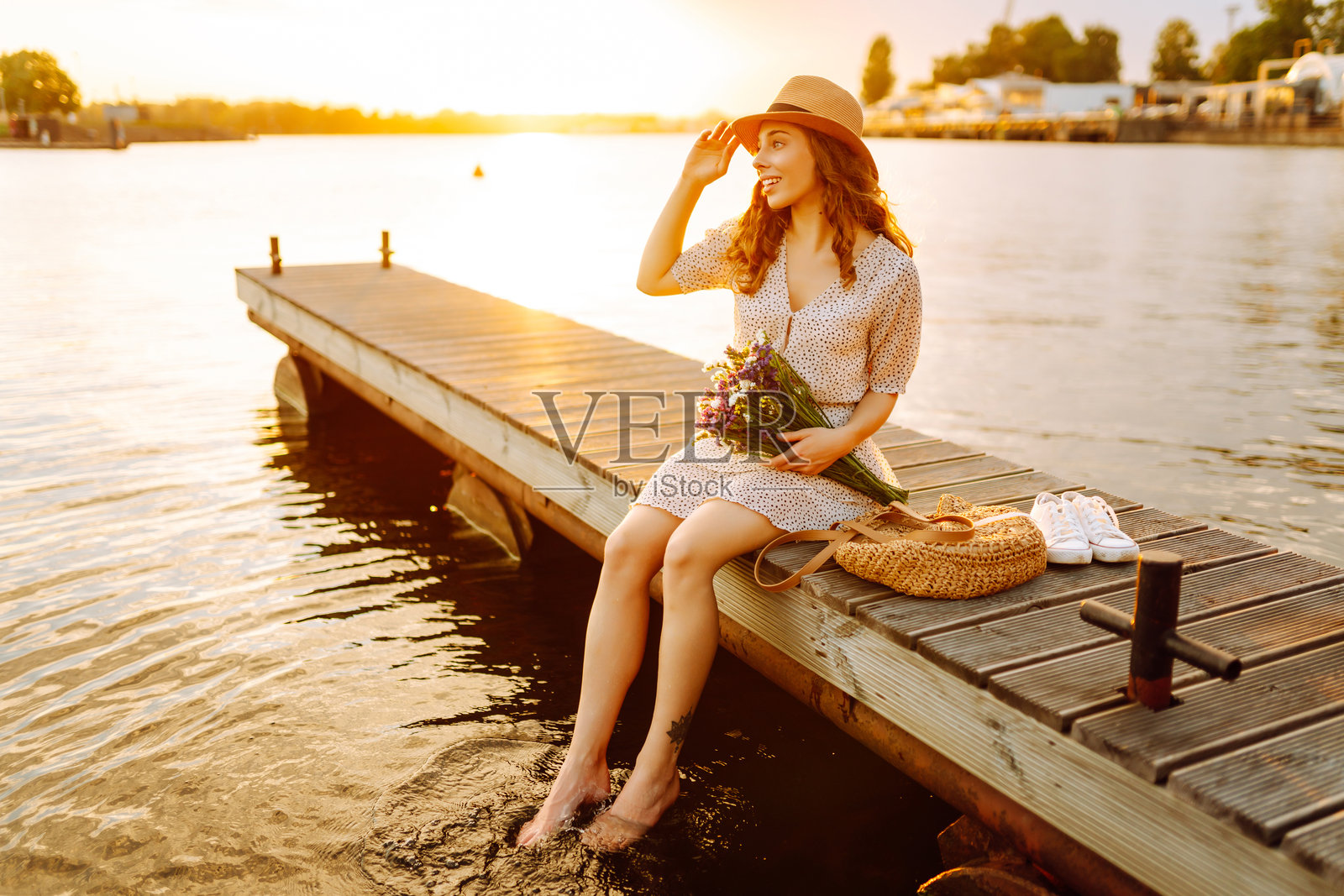 美丽的女人坐在木栈道上，手捧五彩缤纷的花束，夕阳西下。照片摄影图片