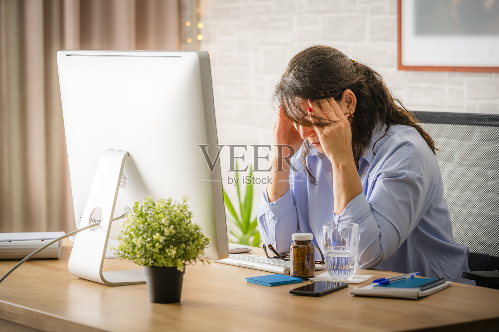 女人疲惫不堪、过度劳累，坐在办公桌旁，双手托着头。照片摄影图片