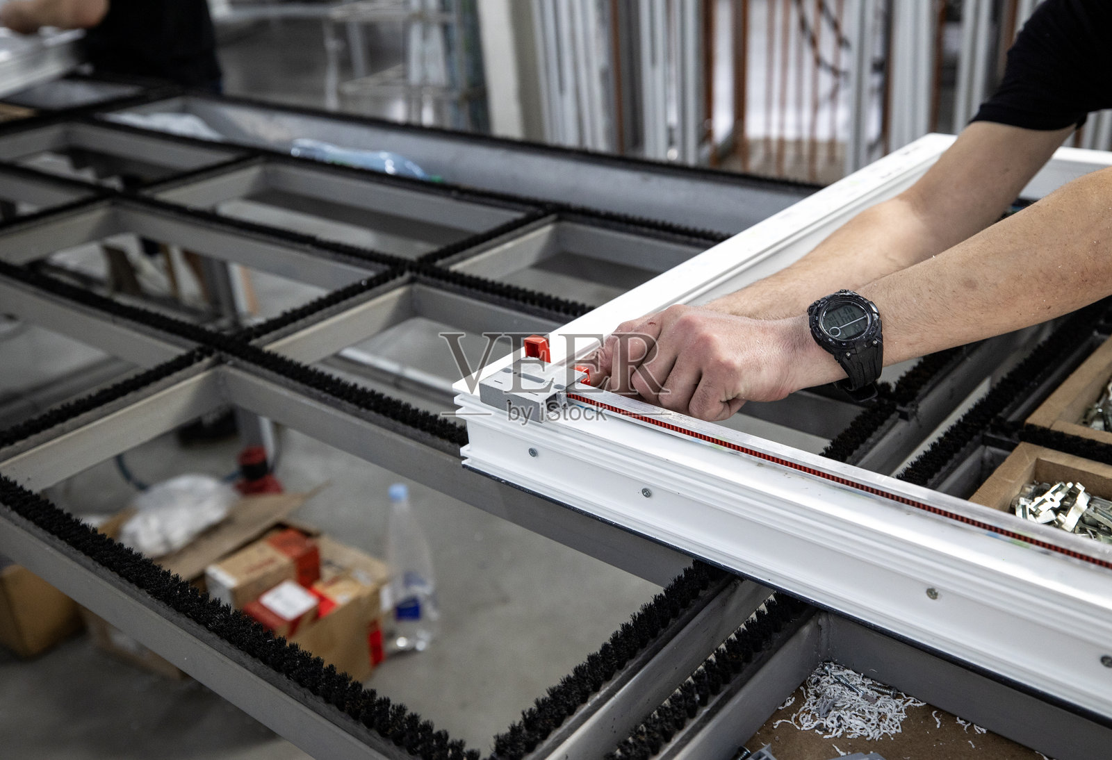 金属塑料或PVC窗户的生产区域，通常称为乙烯窗户。一名工人正在使用红色夹具和固定工具在窗框上安装锁具。照片摄影图片