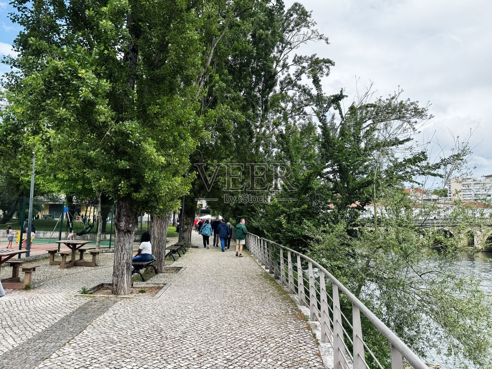 汤马尔风景如画的河边步道,绿树成荫,游客悠闲自在。照片摄影图片