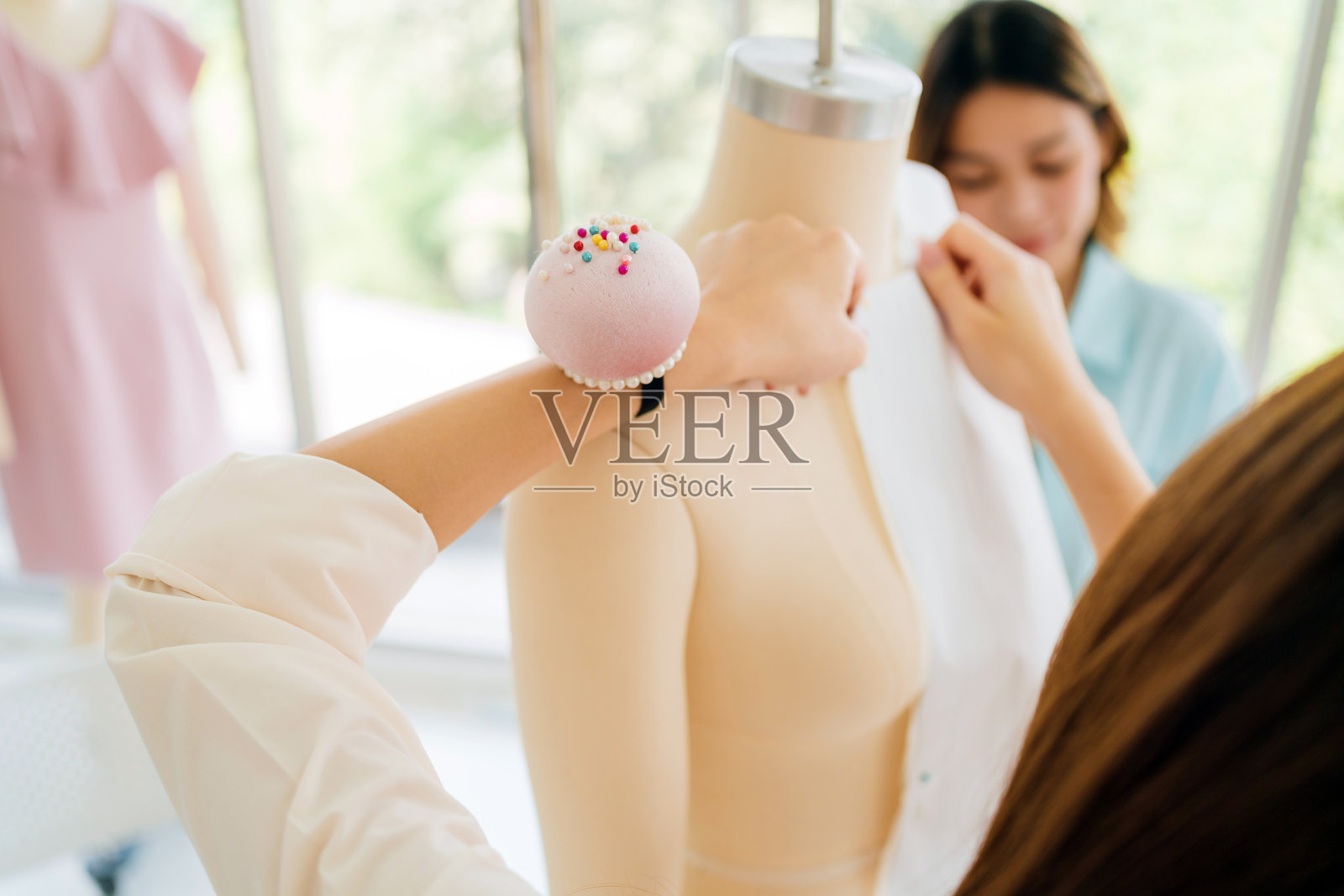 时尚设计师在明亮的工作室中为模特试衣，手腕上戴着针垫，特写镜头。理想的创意、小型企业和手工服装生产概念。照片摄影图片