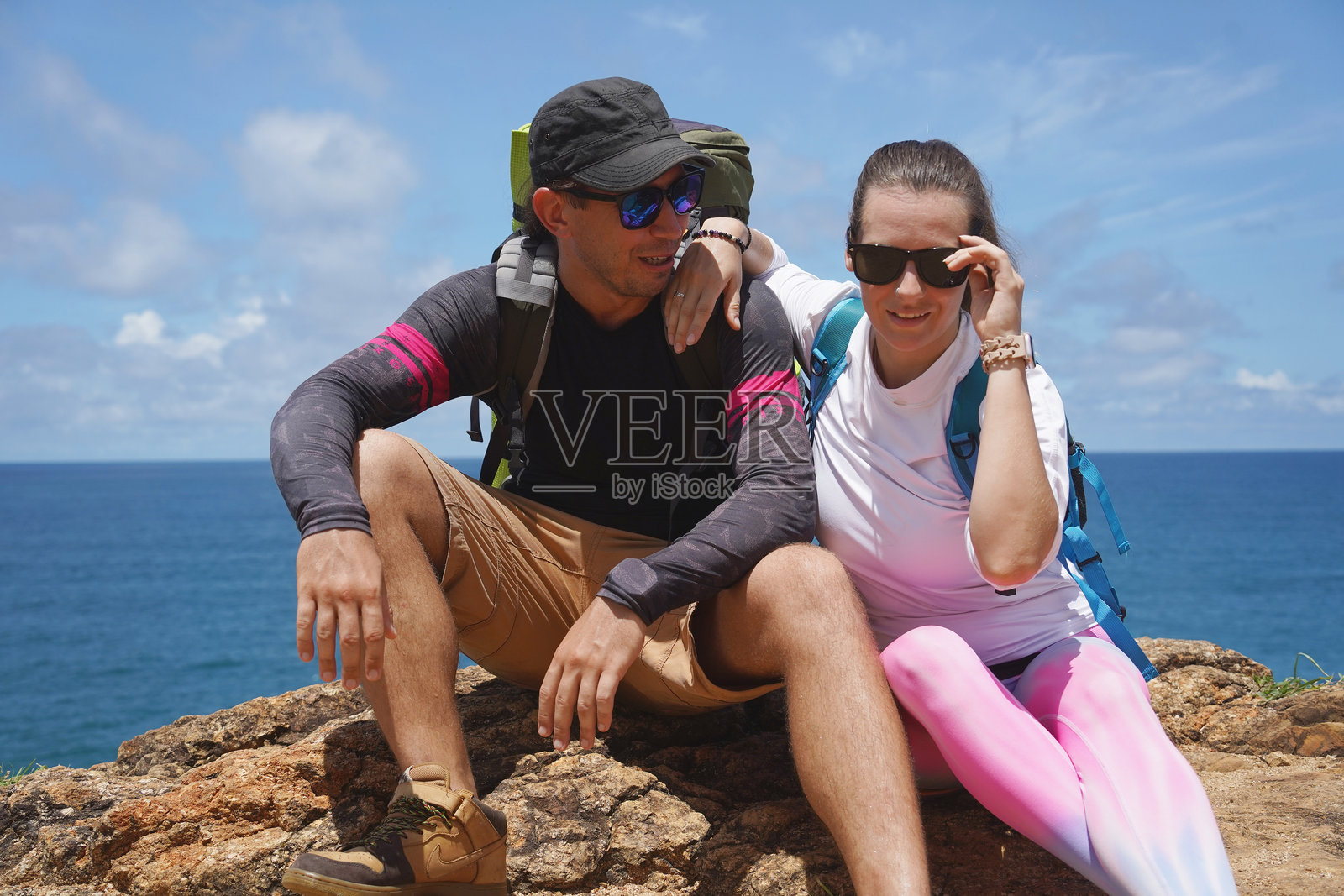 一对年轻情侣在崎岖的岩石悬崖上徒步旅行，俯瞰着海洋的美景。照片摄影图片