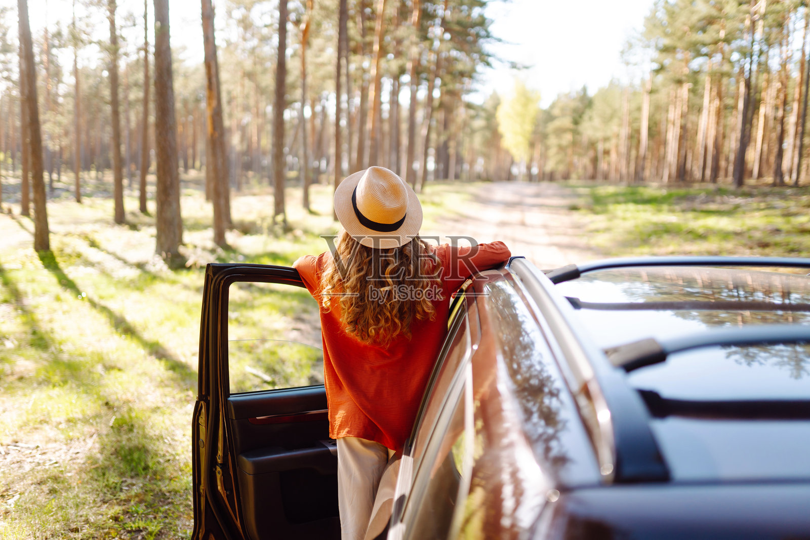快乐的年轻女性站在打开的车门旁，享受森林中的日落。照片摄影图片
