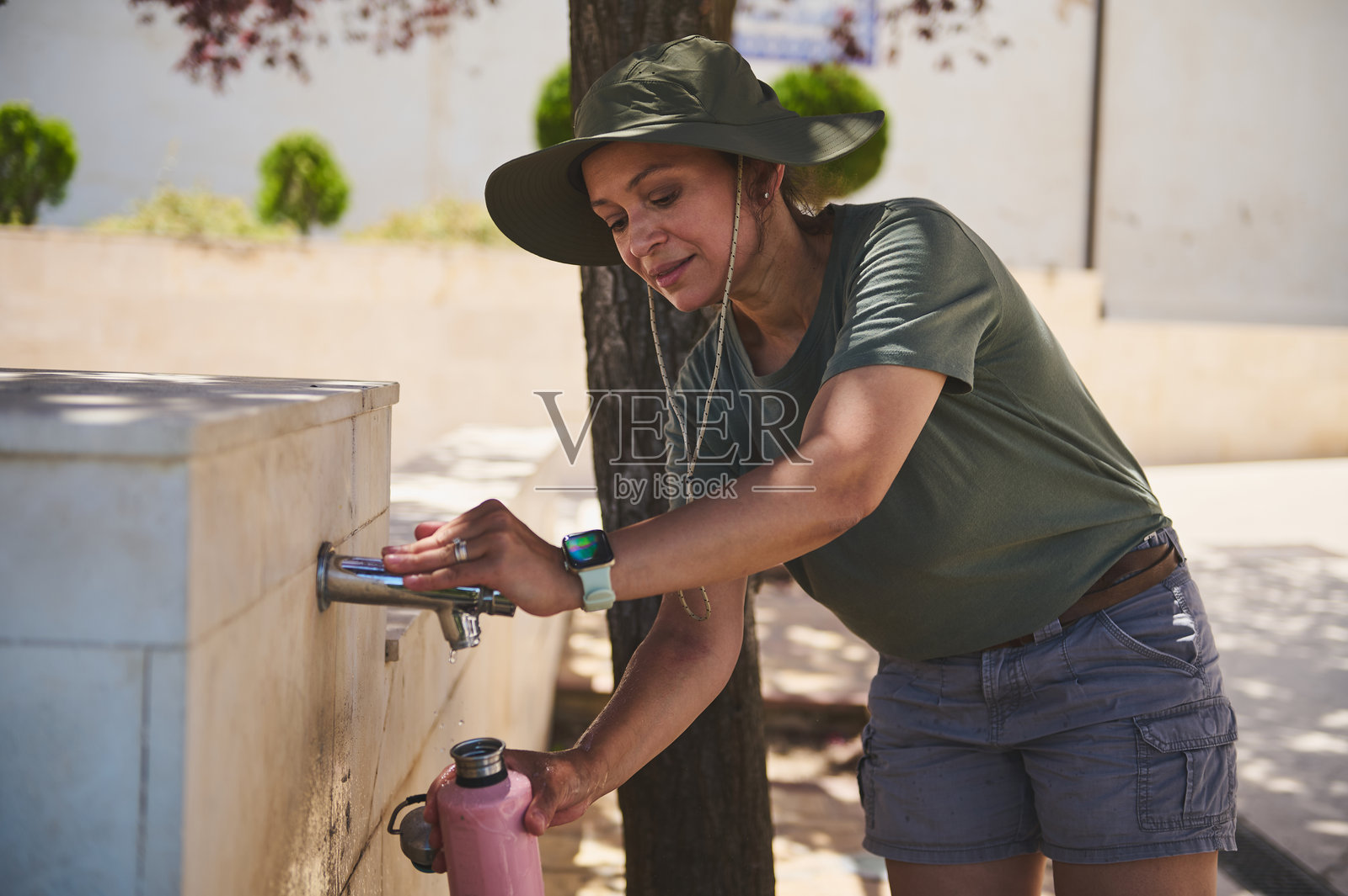 旅行者在阳光明媚的日子里在户外喷泉给水瓶加水照片摄影图片