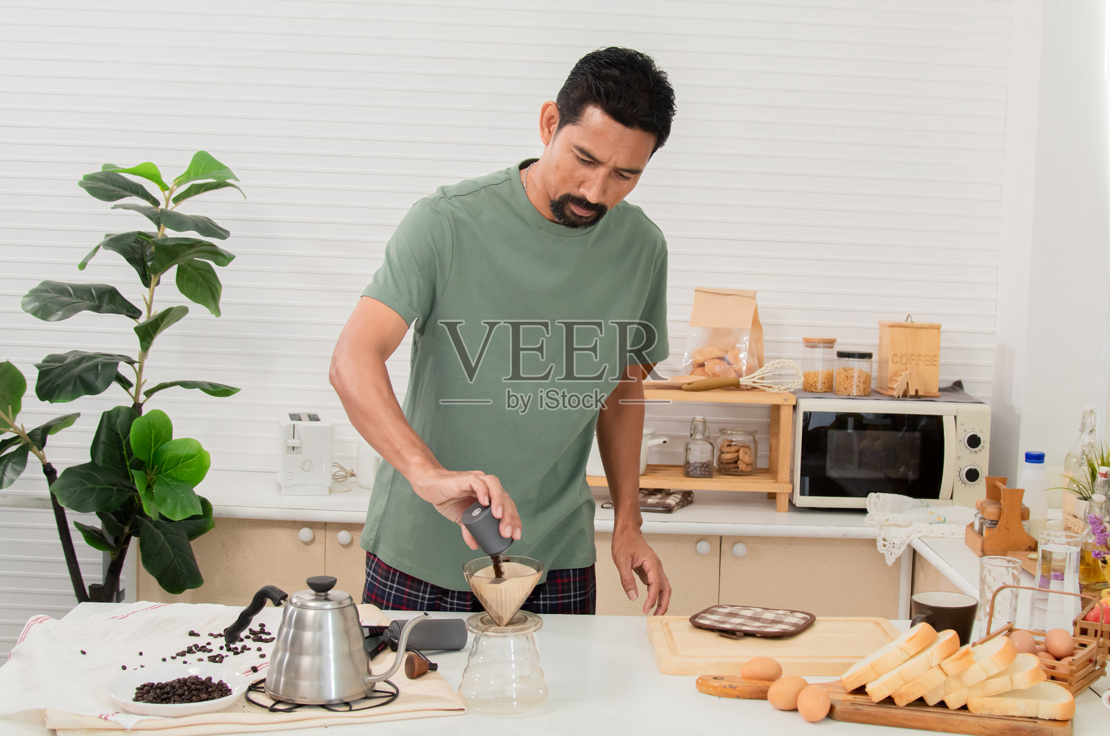 中年有胡子的亚洲男子在家中使用手摇咖啡磨豆机研磨咖啡豆，将其磨成粉，以便早晨饮用。健康生活方式概念。照片摄影图片