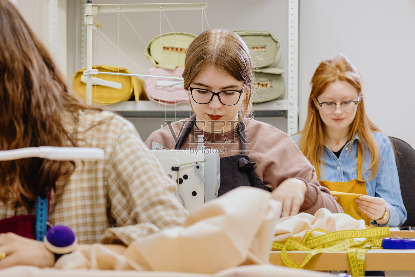 三位女性在服装厂的车间里缝纫，工业设备和缝纫机。照片摄影图片