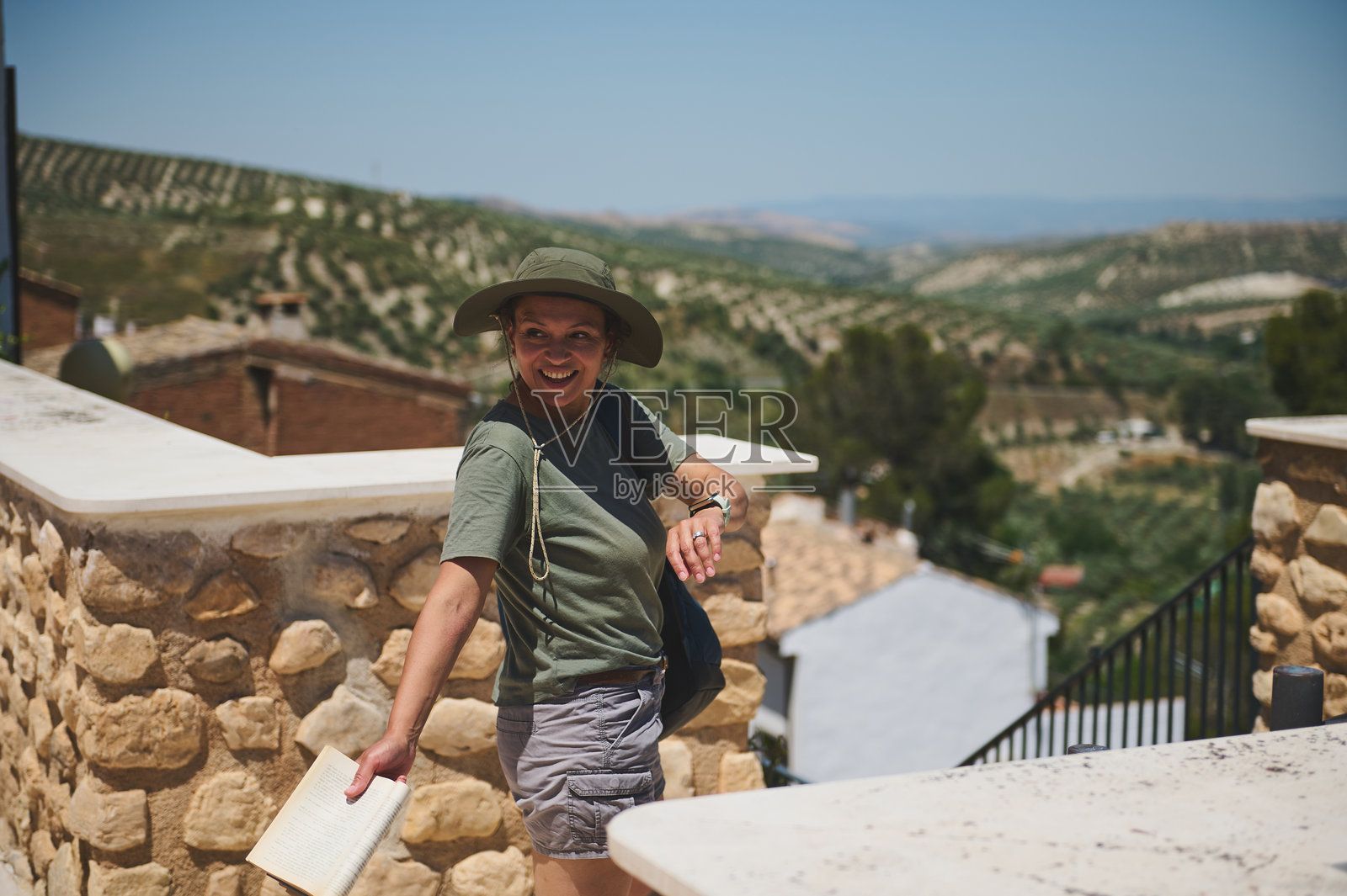 一位女性在乡村风景如画的村庄中探索，手中拿着一本书照片摄影图片