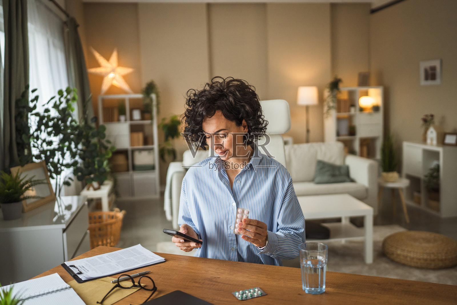 成熟的女性在家中办公室坐着，手持药物并在手机上阅读说明。照片摄影图片