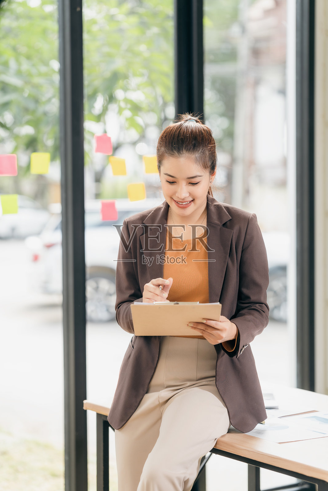 快乐的亚洲女商人在办公室的桌子上微笑着写在夹板上，感到开心和放松，享受在企业工作环境中的工作。照片摄影图片