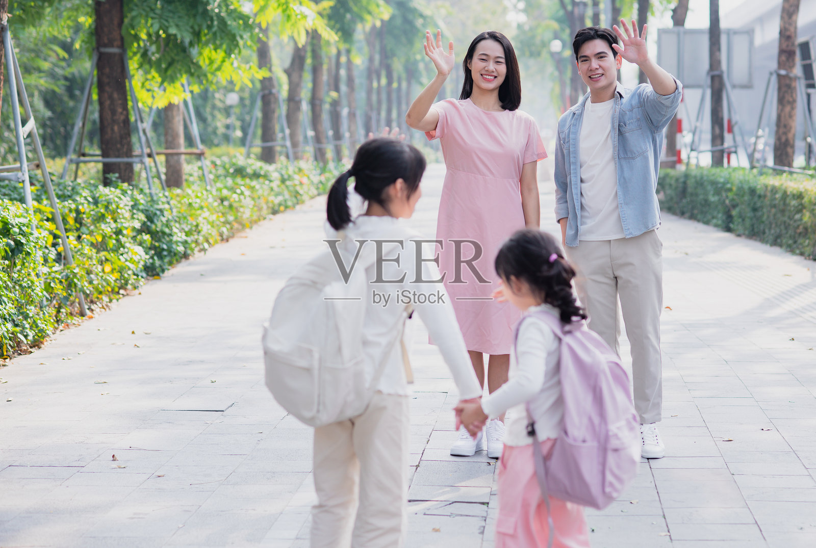 一家人在公园里享受阳光明媚的日子，向微笑的孩子们挥手。照片摄影图片