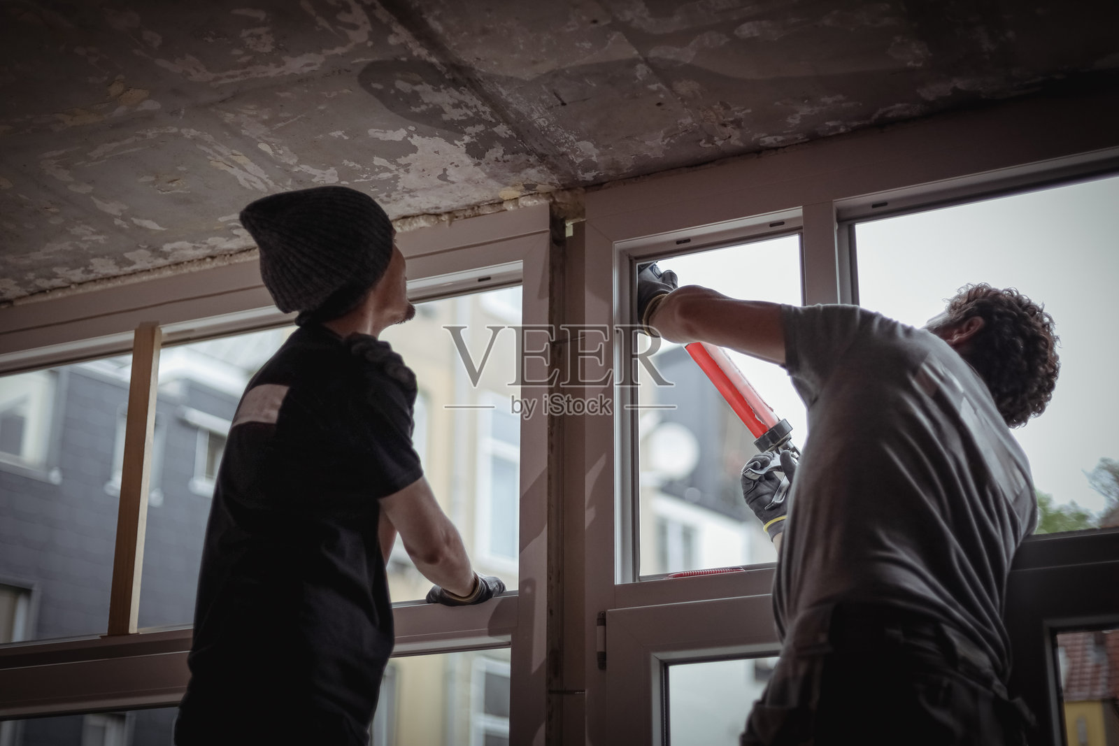 两个人正在修理窗户，用硅胶密封裂缝。照片摄影图片