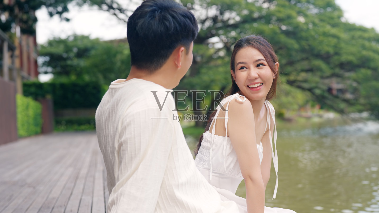 年轻的亚洲情侣在公共自然公园中愉快地交谈，坠入爱河，渴望亲吻和拥抱，彼此关心和信任。甜蜜的亚洲恋人面对面，男士和女士微笑，放松，享受温暖的约会时光。照片摄影图片