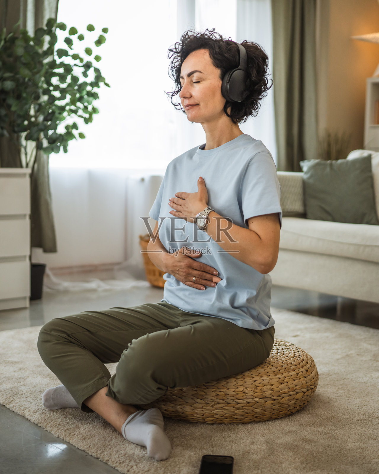 成熟的女性坐在地板上，戴着耳机进行引导冥想。照片摄影图片