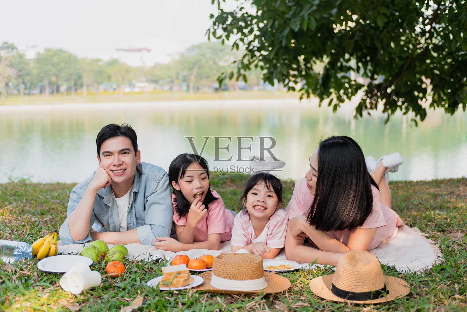 一家人在阳光明媚的下午，在宁静的湖边公园享受野餐，孩子们和水果相伴。照片摄影图片