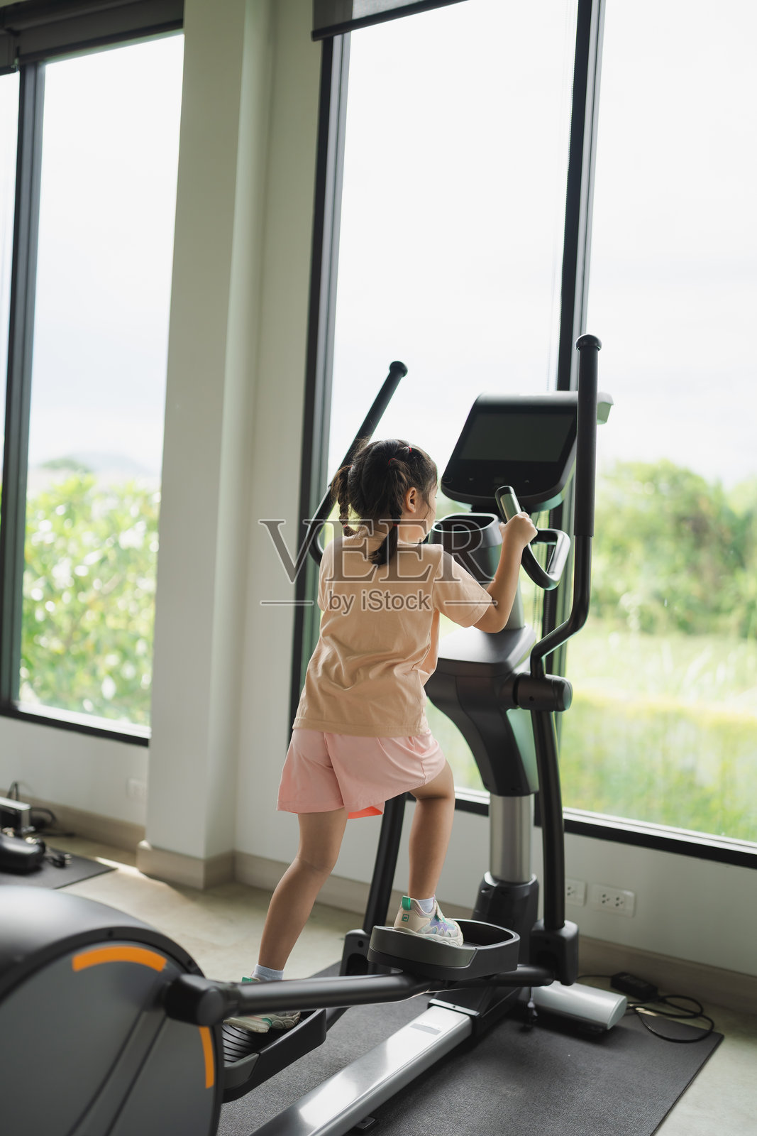 年轻女孩在明亮现代的健身房内使用椭圆机，窗外风景优美。照片摄影图片