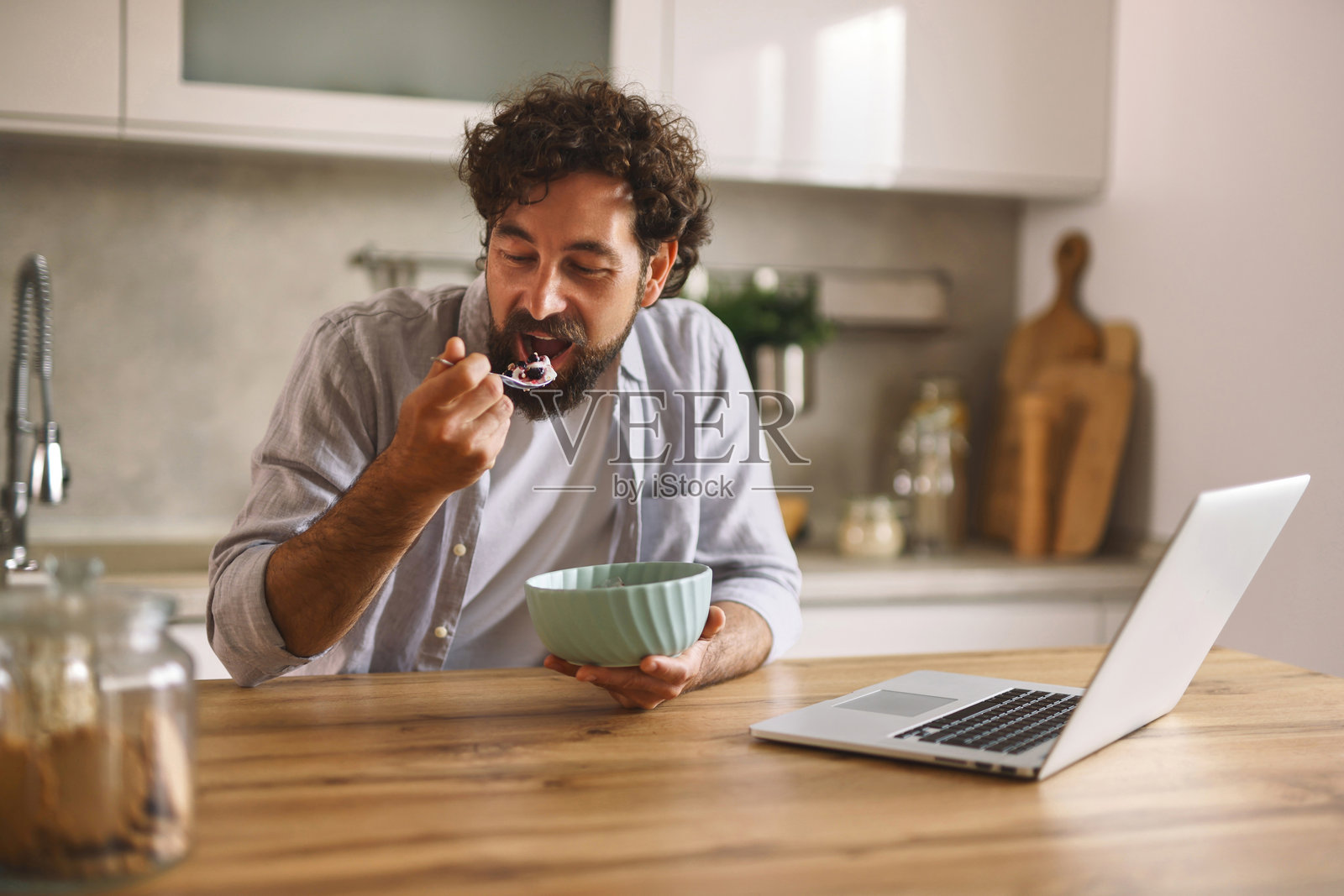 年轻男子在厨房享用早餐并使用笔记本电脑工作照片摄影图片