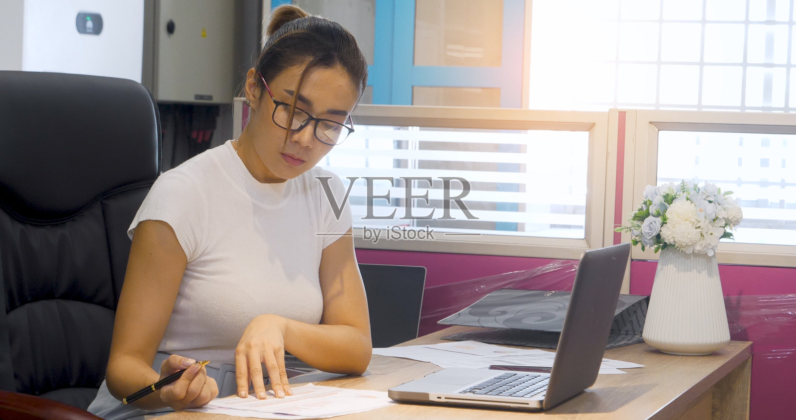 商务女性在办公室桌子上用笔记本写作，同时在笔记本电脑上打字。亚洲女性的手在办公室纸上写计划，使用笔记本电脑上的日历。女性手持笔，进行商业计划工作。照片摄影图片