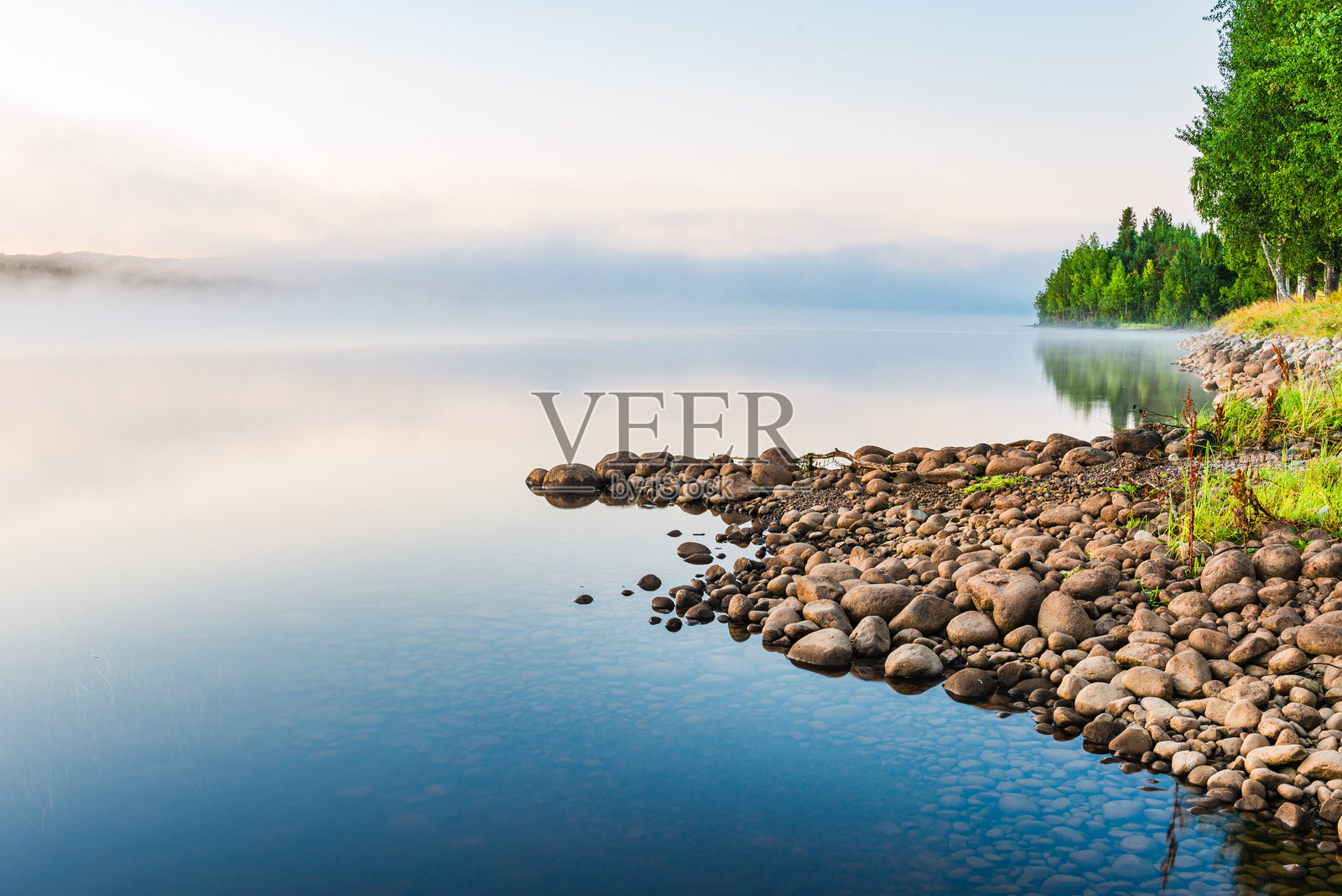 雾气笼罩着瑞典的一片宁静湖泊，营造出宁静的晨间氛围，湖边的石头和倒影交相辉映。照片摄影图片