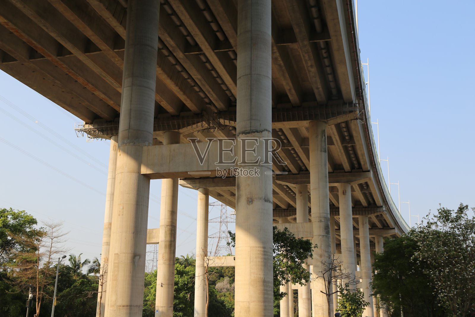 一个有大型混凝土柱子的高速公路立交桥，桥下是一个工业园区，正午时分阳光从上方照射下来。照片摄影图片