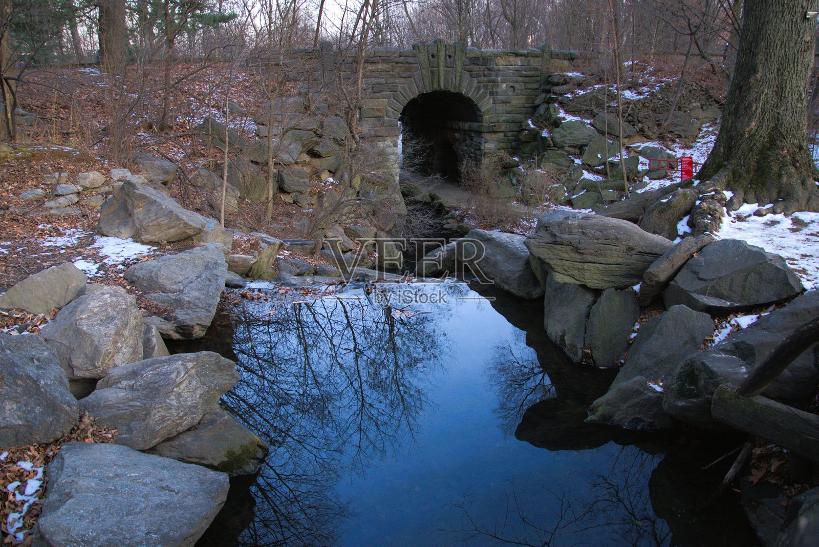 一条狭窄的湖泊，水流在大石头之间穿行，并流过一座桥。照片摄影图片