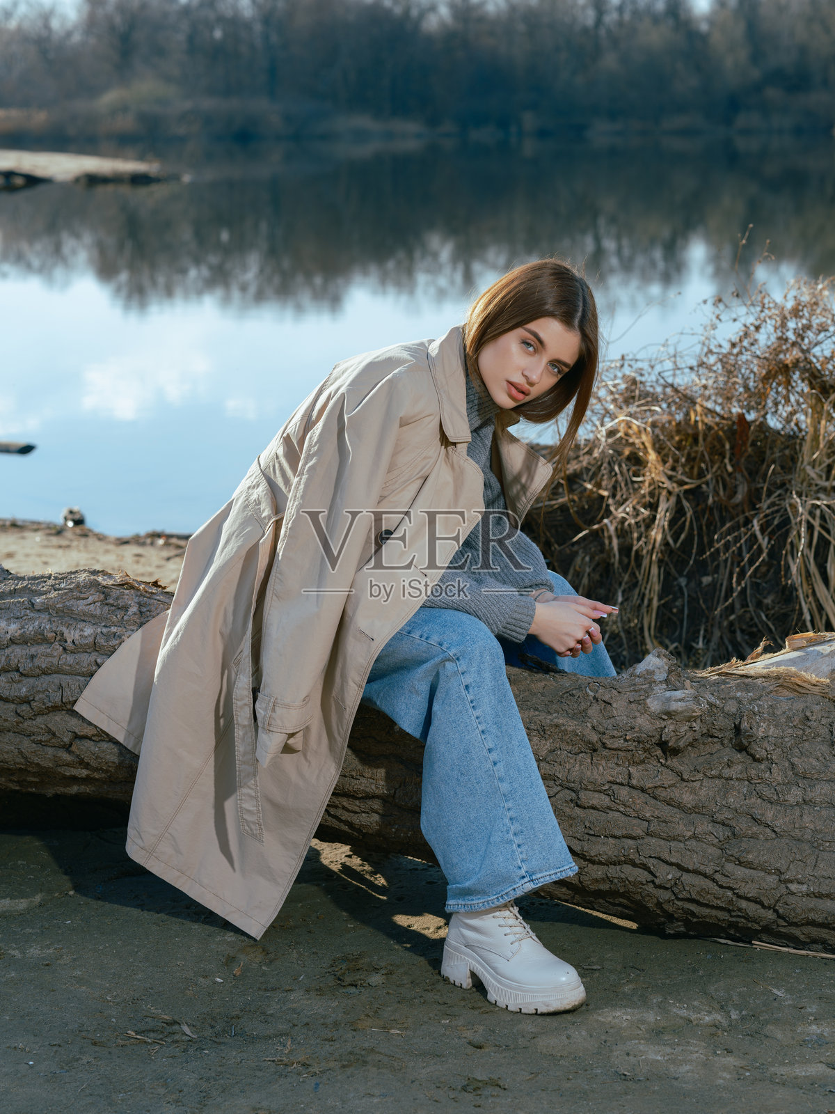 年轻女性坐在湖边的原木上，平静的湖水映照着天空和云朵。照片摄影图片