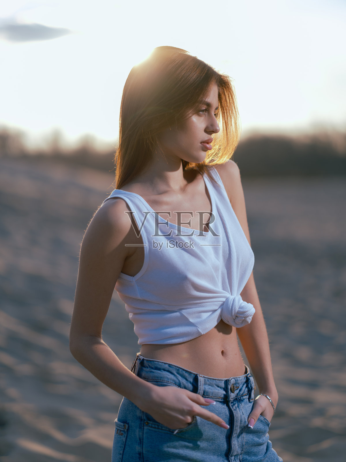 年轻的棕发女性站在海滩上，背后是日落时分的沙滩和天空。照片摄影图片