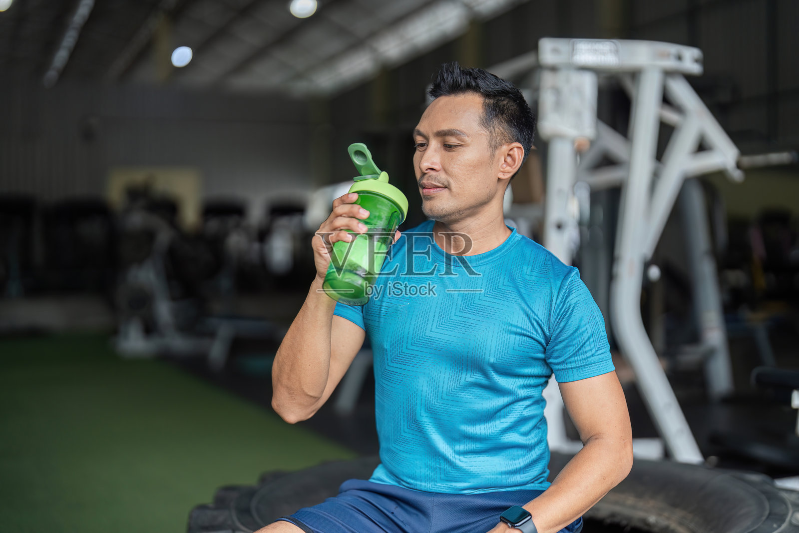 健身补水。一名男子在健身房享受他蛋白质摇摇杯中的饮料。照片摄影图片