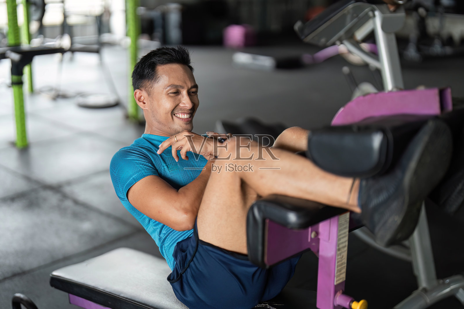 快乐健身。男子在健身器械上微笑进行腿部锻炼。照片摄影图片